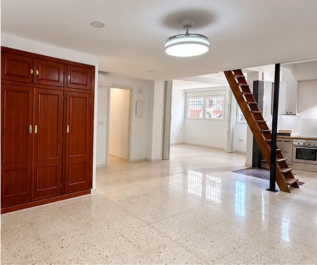 Salón con cocina abierta y escalera al altillo del piso reformado en Barrio del Naranjo